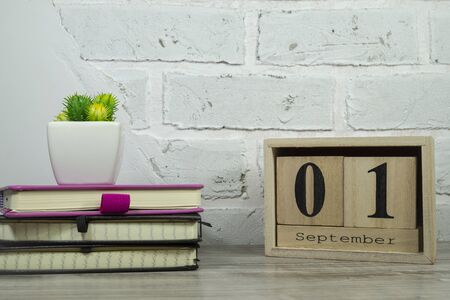 September still life with books, potted plant and rustic sign for the month against a white brick...