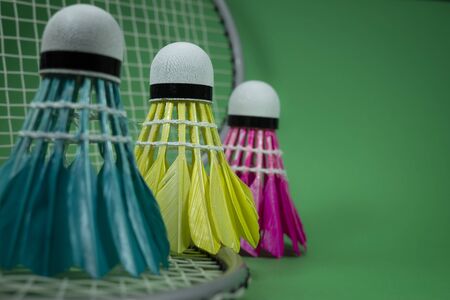 Badminton rackets and colorful feathered shuttlecocks in blue, yellow and pink on green background in a close up viewの写真素材
