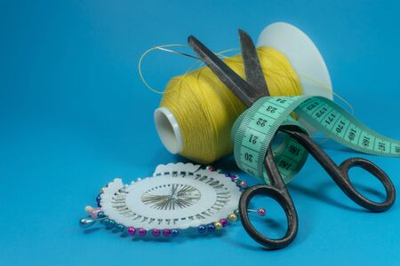 Old metal scissors wrapped around with tape measure and spools of thread on blue background, needlework and tailoring concept with free copy spaceの写真素材
