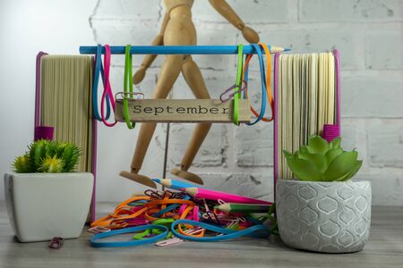Colorful September still life with potted plants, a pile of pencils and rubber bands and rustic sign for the month in front of a wooden figure against a white brick wallの写真素材