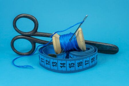 A close up image of a tape measure, old metal scissors, spool of blue thread and sewing needle on...