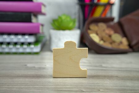 Wooden puzzle piece standing on end on a table with blurred background of books and open purseの写真素材