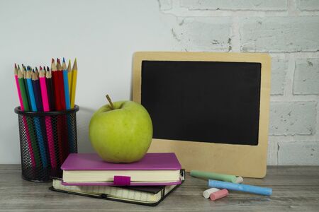 September still life with pile of books, green apple, pencils and chalk board against a white brick wall with free copy spaceの写真素材