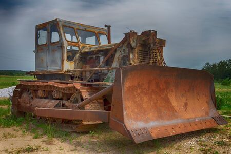 Low angle view of an old rusty heavy duty industrial digger or grader parked outdoors in a field...