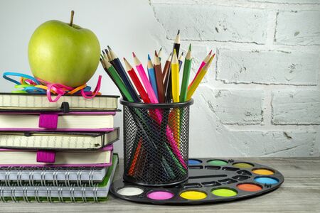 Back to school concept with pile of books, green apple and pencils against a white brick wall with free copy spaceの写真素材