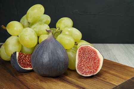 Fresh tropical fruit still life with juicy ripe purple figs and bunches of red and green grapes on a...