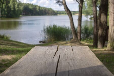 Old cracked weathered wooden picnic table outdoors overlooking a tranquil like or river with shady treesの写真素材