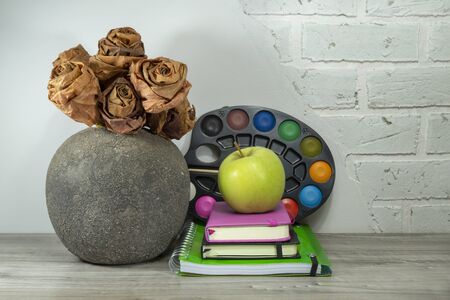 Back to school concept with pile of books, green apple and solid watercolors paints against a white brick wall with free copy spaceの写真素材