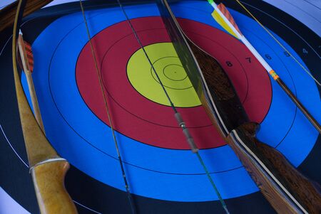 Bow and arrow with an archery target in a close up oblique angle view in a concept of goals, skill, sport and precisionの写真素材