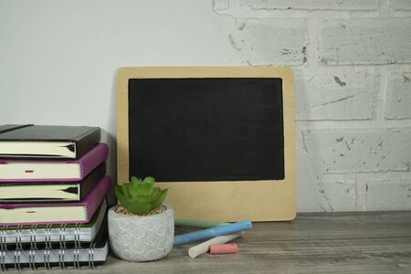 September still life with pile of books, potted plant, chalks and chalk board against a white brick wall with free copy spaceの写真素材