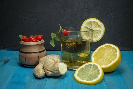 Still life with ingredients for a healthy infusion with fresh root ginger, lemon, garlic and rose hips together with a steaming glass of tisane over a blue backgroundの写真素材