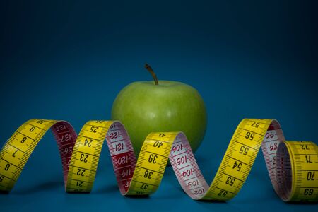 Weight loss and healthy diet concept with measuring tape and green apple on blue backgroundの写真素材