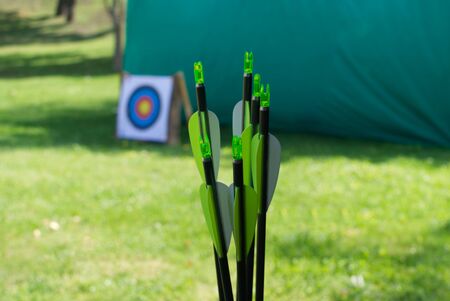 Close up on the green flights of arrows outdoors in a field with a tent and target visible behind in the sunshineの写真素材