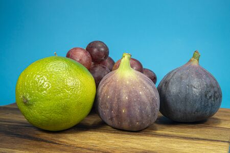 Fresh tropical fruit still life with juicy ripe purple figs, lime and bunches of red grapes on a wooden tableの写真素材