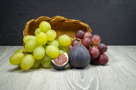 Fresh tropical fruit still life with juicy ripe purple figs and bunches of red and green grapes on a wooden tableの写真素材