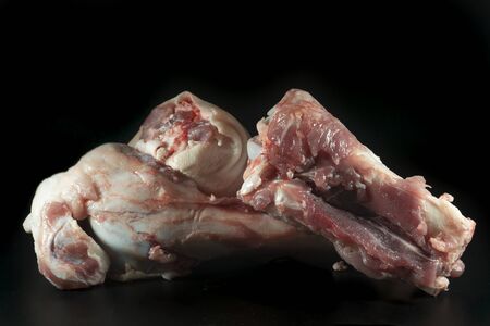 Two raw knuckle or joint bones on black, one with skin covering the bone and copy space above