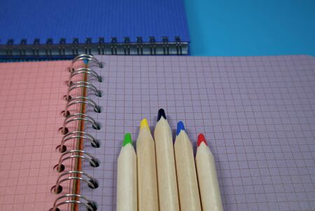 Pencils crayons lying on wire bound open notebook ruled with squares with green and purple pages in a conceptual image for business or educationの写真素材