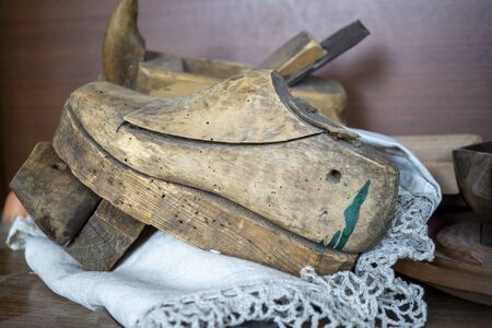 Old vintage wooden shoe mold or last on a lacy mat on a workbench with assorted tools behind in a close up side viewの写真素材