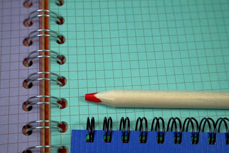 Pencil crayon lying on wire bound open notebook ruled with squares with green and purple pages in a conceptual image for business or educationの写真素材