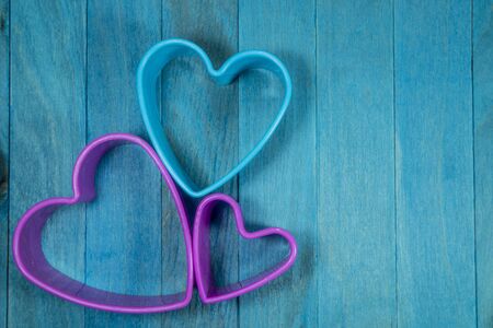 Colored heart-shaped cookie cutter figures forming a decorative flower, sitting on blue wooden background and viewed from aboveの写真素材