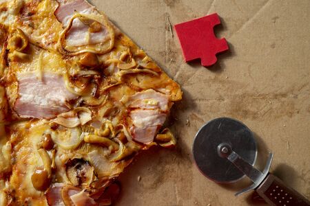 Slice of tasty traditional Italian pizza with pastry wheel and bright red puzzle piece on a marble...