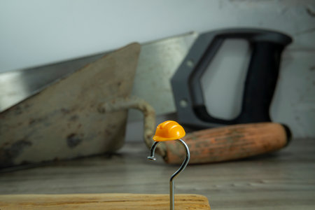 Construction nail shaped as question mark with yellow plastic workplace helmet and blurred...