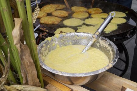 Autumn pumpkin batter for making seasonal fritters in a large metal bowl with spoon and pancakes or fritters cooking on an outdoor griddle behind, conceptual of the seasonsの写真素材