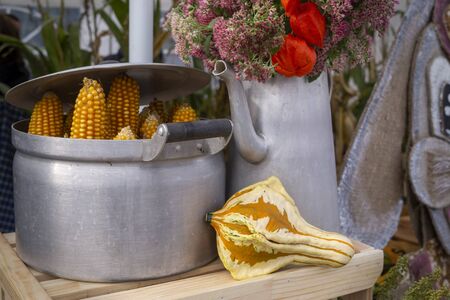 Autumn still life with dried corncobs in a metal pot and ornamental gourd in front of an old watering can filled with colorful flowers conceptual of the seasonsの写真素材