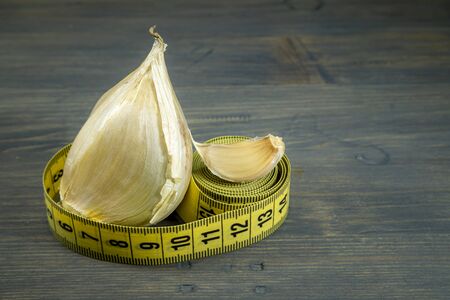 Elephant garlic (Allium ampeloprasum) regular garlic cloves and tape measure on a rustic wooden tableの写真素材