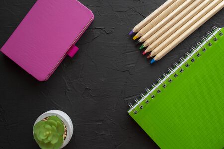 Back to school background with green spiral ring bound notebook, pink notebook and pencils on black background. Flat lay, view from aboveの写真素材