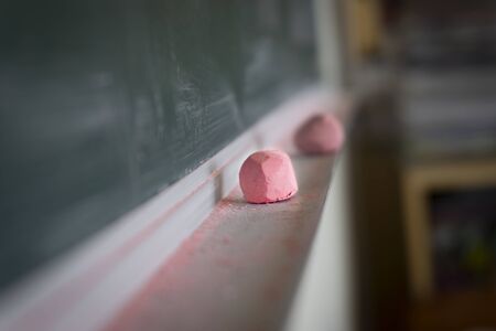 Pink chalk and eraser on the shelf below a chalkboard or blackboard in a classroom in a low angle selective focus view with copy spaceの写真素材