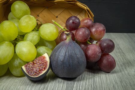 Fresh tropical fruit still life with juicy ripe purple figs and bunches of red and green grapes on a wooden tableの写真素材