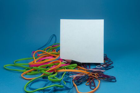Pile of colorful rubber bands over blue background with a white sheet of note paper for textの写真素材