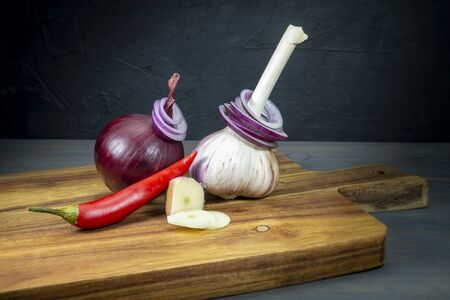 Red onion, whole and sliced in rings, garlic and chili pepper vegetables, sitting on wooden cutting board and viewed in closeup, from high angleの写真素材