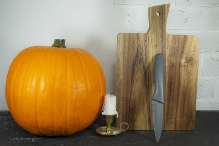 Autumn pumpkin with chefs knife and cutting board with a small vintage brass candlestick and used extinguished candle in a seasonal still lifeの写真素材