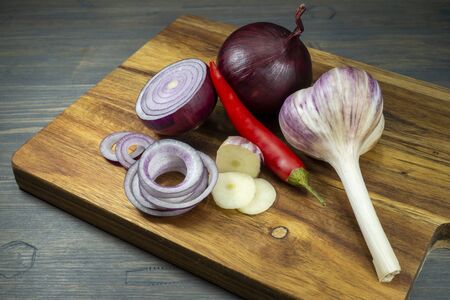 Red onion, whole and sliced in rings, garlic and chili pepper vegetables, sitting on wooden cutting board and viewed in closeup, from high angleの写真素材