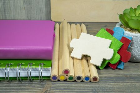 Back to school concept with colorful wooden puzzle pieces, books and pile of pencils on the table against a grey wall with free copy spaceの写真素材
