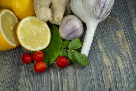 Natural remedies for cold and flu season with fresh root ginger, lemon, garlic and rose hips on a rustic wooden tableの写真素材