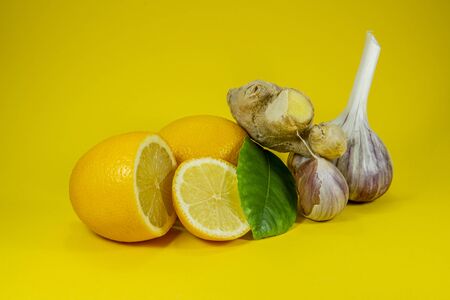 Ingredients for a healthy infusion with whole and sliced lemon with green leaf, fresh root ginger and garlic over a yellow background, natural remedies for cold and flu seasonの写真素材