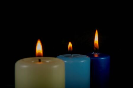 Close up of three colorful wax candles flame on a dark background with copy spaceの写真素材