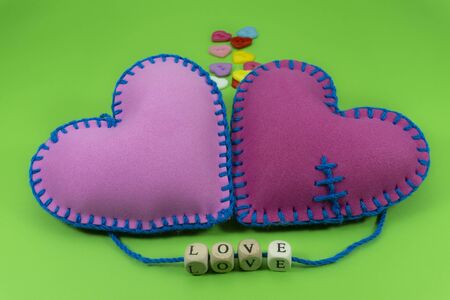 Hand stitched textile hearts with word Love on blocks threaded on strings over a colorful green background for romantic relationship, Valentines Day, broken heart conceptの写真素材