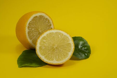 Halved ripe lemon fruit with green leaves on yellow backgroundの写真素材