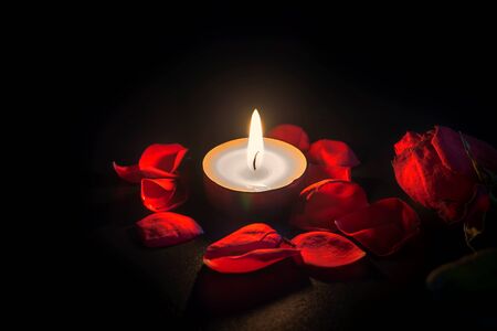 Tea candle and red rose petals with shallow depth of focus with reflection on black backgroundの写真素材