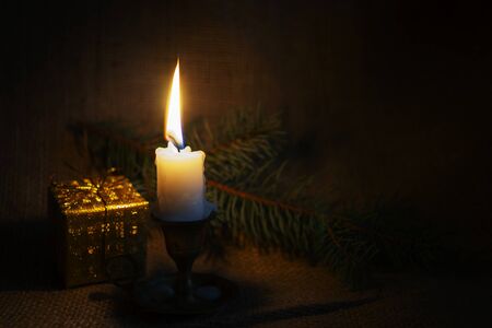 Christmas background with burning candle, gift and fir branch on rustic burlap background with copy space for a holiday greetingの写真素材