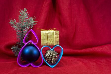 Christmas decorations with plastic hearts and small golden present box on red fabric background with copy spaceの写真素材