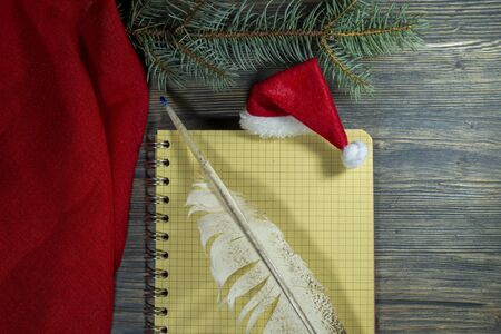 Red Santa hat with quill pen and spiral bound notebook decorated with a border of red fabric and pine branch for Christmas themed conceptsの写真素材