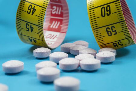 Medicine pills and measuring tape on blue background. Healthcare, diet or weight loss conceptの写真素材