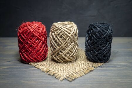 Three balls of natural hemp twine with coarse fibers in a natural brown, red and black with a square...