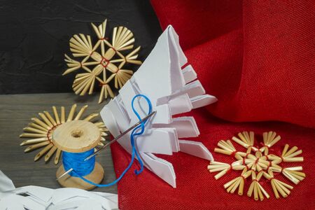 Festive Xmas background with homemade Christmas decorations from straw, crocheted string and paper alongside red fabric and a pair of scissorsの写真素材