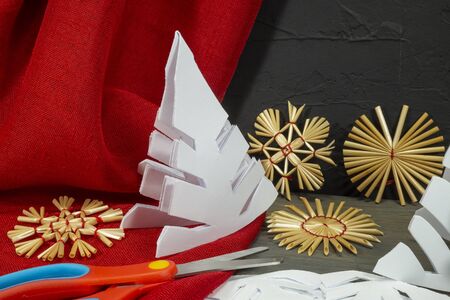 Festive Xmas background with homemade Christmas decorations from straw, crocheted string and paper alongside red fabric and a pair of scissorsの写真素材